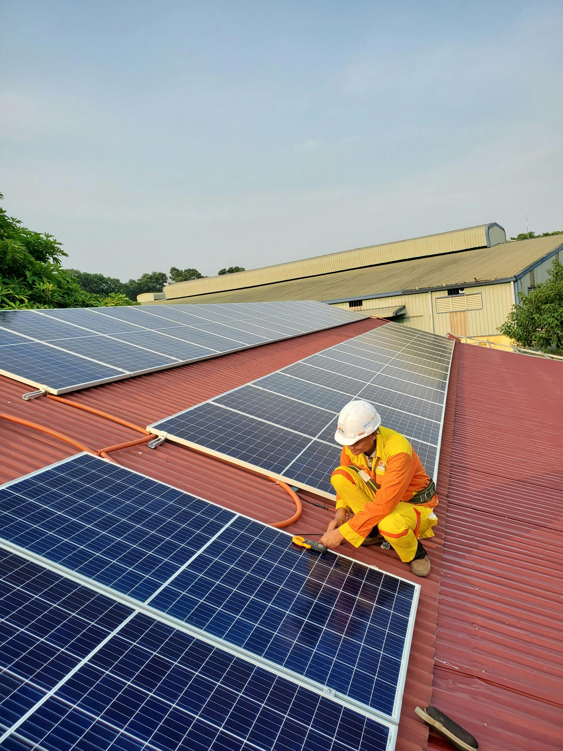 pexels-photo-14613939-14613939 Technician working on solar panel installation on a rooftop under clear sky.