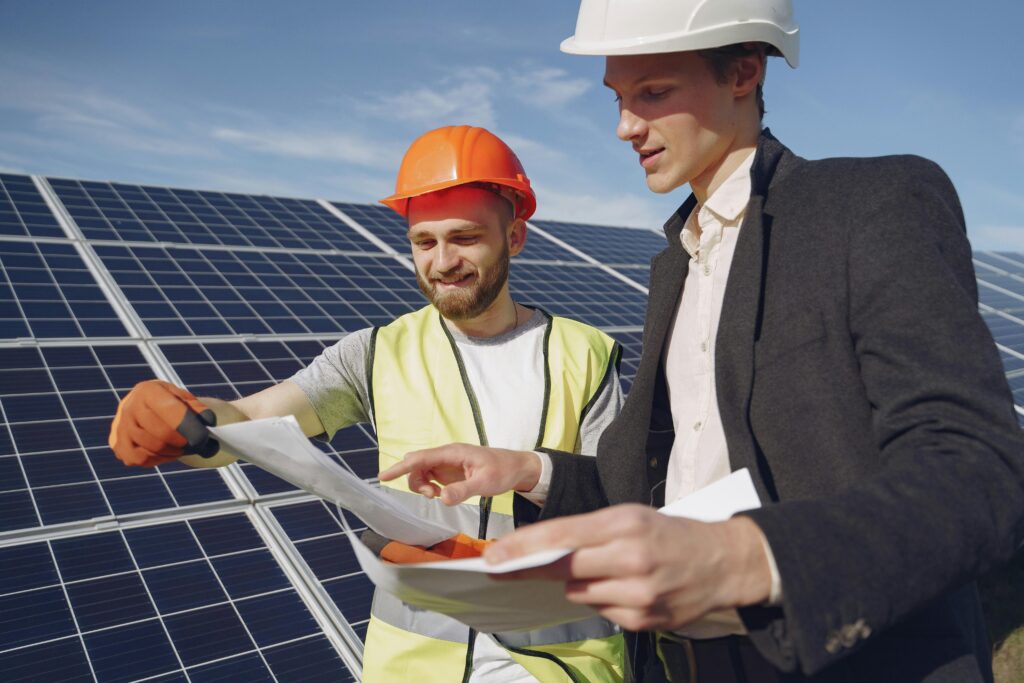 pexels-photo-4254157-4254157 Two engineers reviewing plans for solar panel installation, representing teamwork in renewable energy.